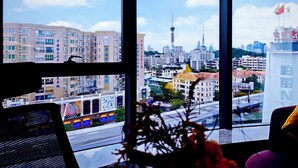 Vista da janela com vista para um horizonte urbano com edifícios modernos, uma torre imponente e um letreiro do McDonald's.