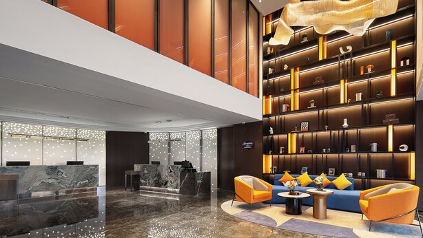 Un moderno vestíbulo de hotel con mostrador de recepción, zona de estar y una amplia estantería.
