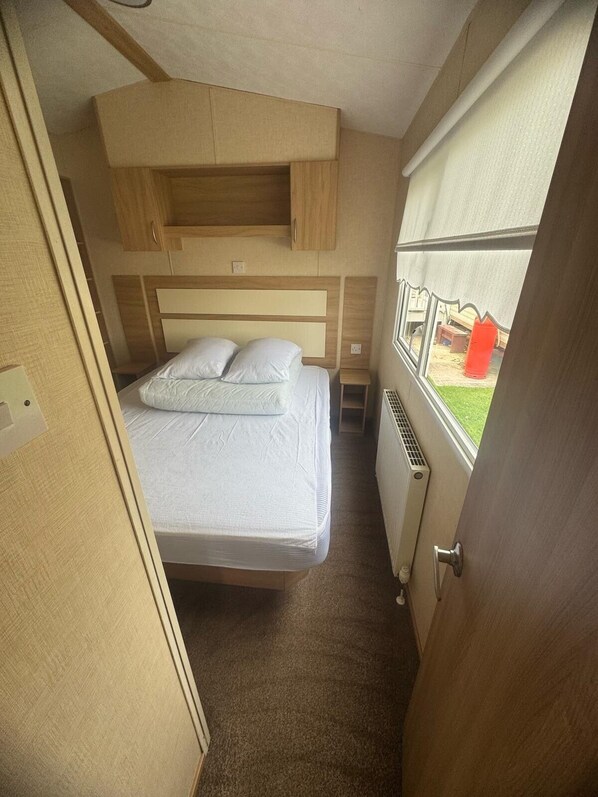 A compact bedroom with a bed, wooden headboard, and a window with a view of the outside.