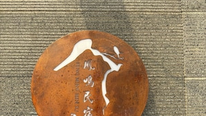 A round, rust-colored plaque with Chinese characters and a number '106' on a textured wooden background. Below it, a blue sign with white text also displays the number '106'. - Feng Ming home stay (Jinning)