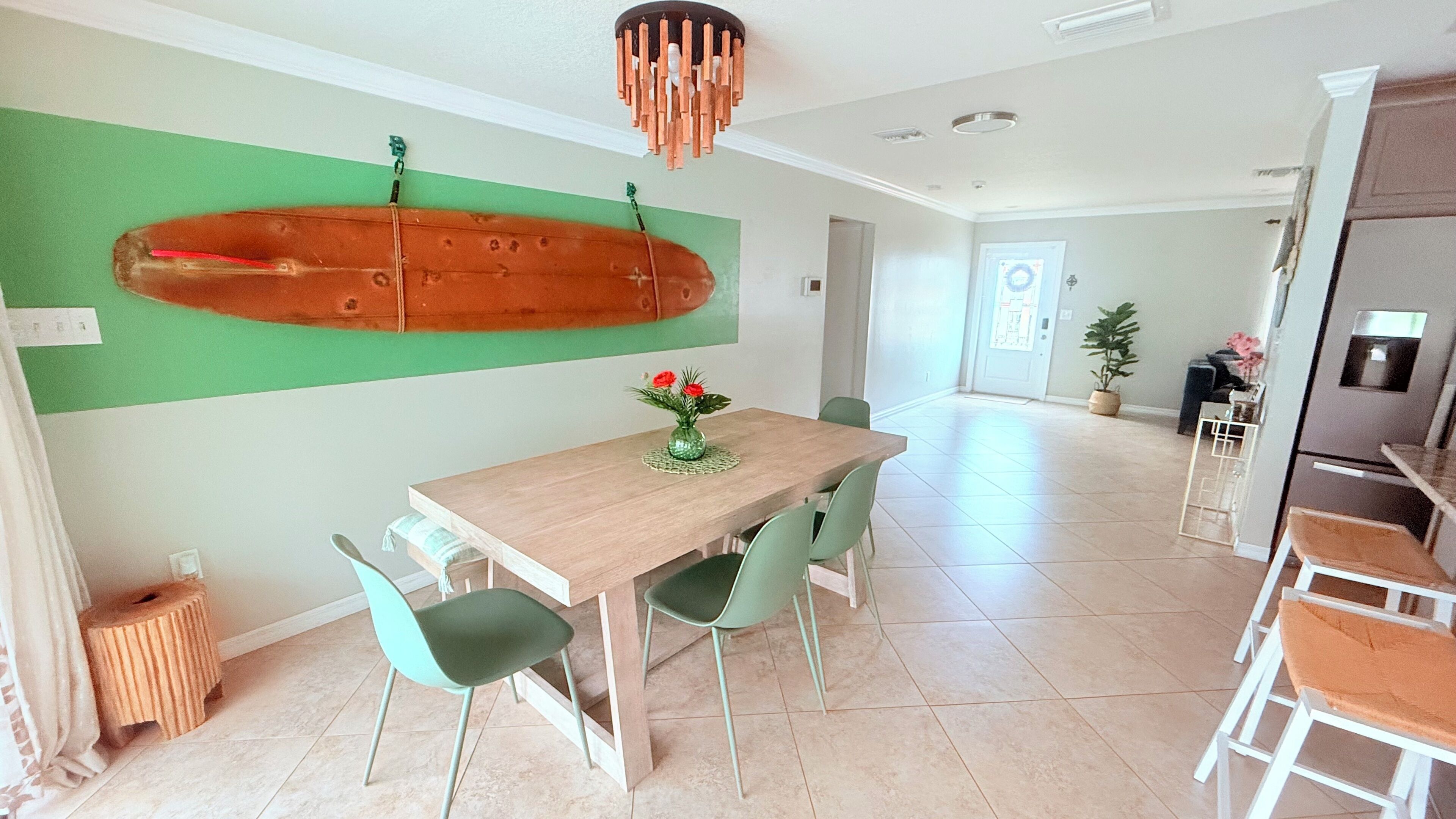 A modern kitchen with a wooden dining table, green chairs, and a hanging light fixture.