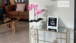 A living room with a modern design, featuring a glass coffee table, a brown sofa, and decorative wall art.