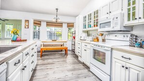 Une cuisine avec des armoires blanches, un banc en bois et une grande fenêtre.