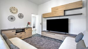 A modern living room with a flat-screen TV, wooden storage units, and decorative clocks on the wall. - La Siesta with Private Garden, Torre del Lago, Italy (Torre del Lago)