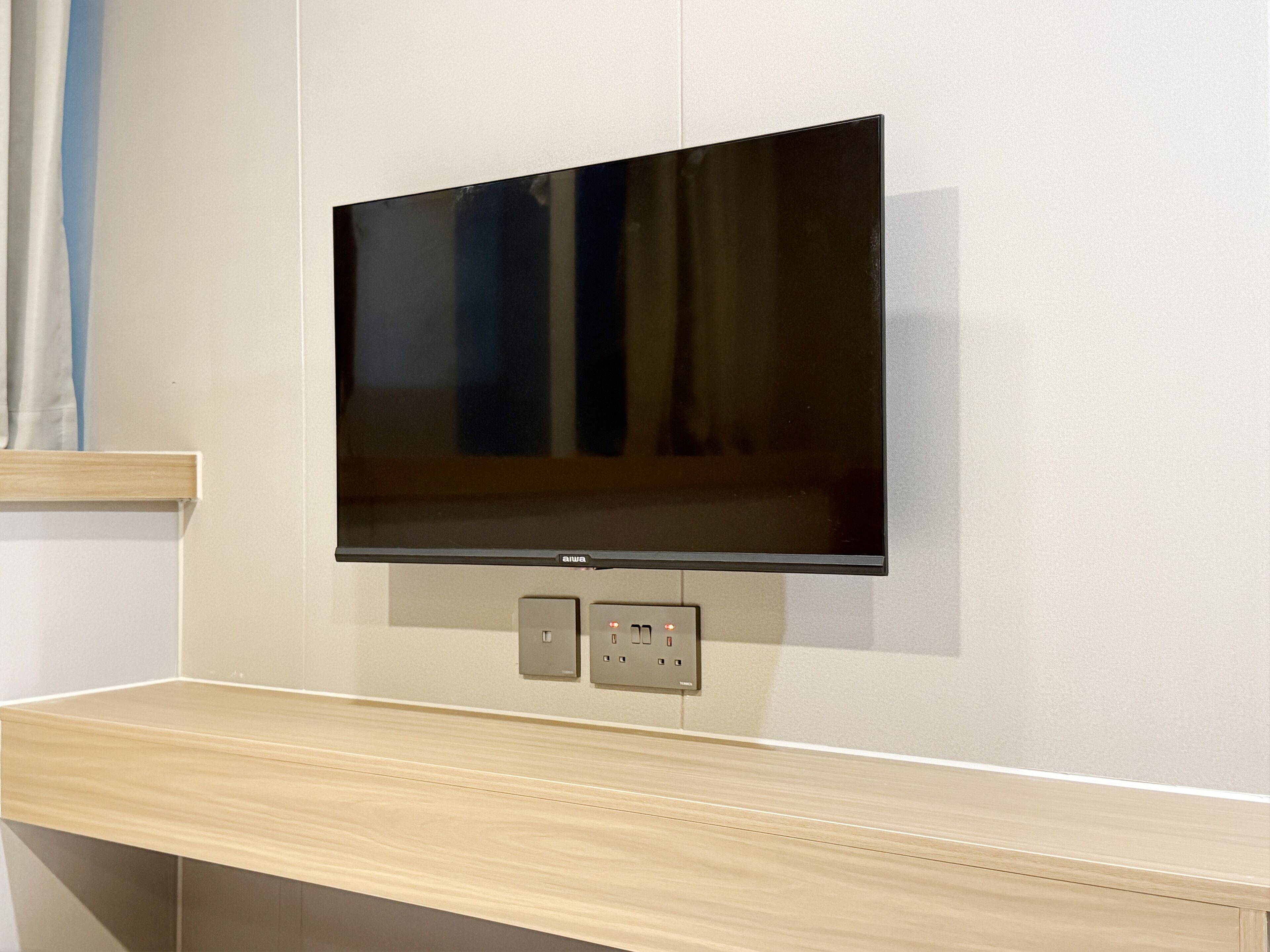 Un televisor de pantalla plana montado en la pared con un estante de madera debajo.