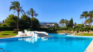 A swimming pool with steps leading into it, surrounded by palm trees and a stone wall.