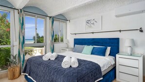 A bedroom with a bed, a nightstand, a window with curtains, and a view of greenery outside.