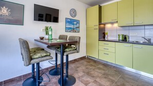 A modern kitchen with green cabinets, a dining area with bar stools, a flat-screen TV, and a painting on the wall.