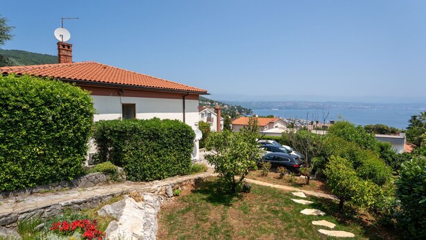 A house with a red-tiled roof, a satellite dish, and a view of the sea.