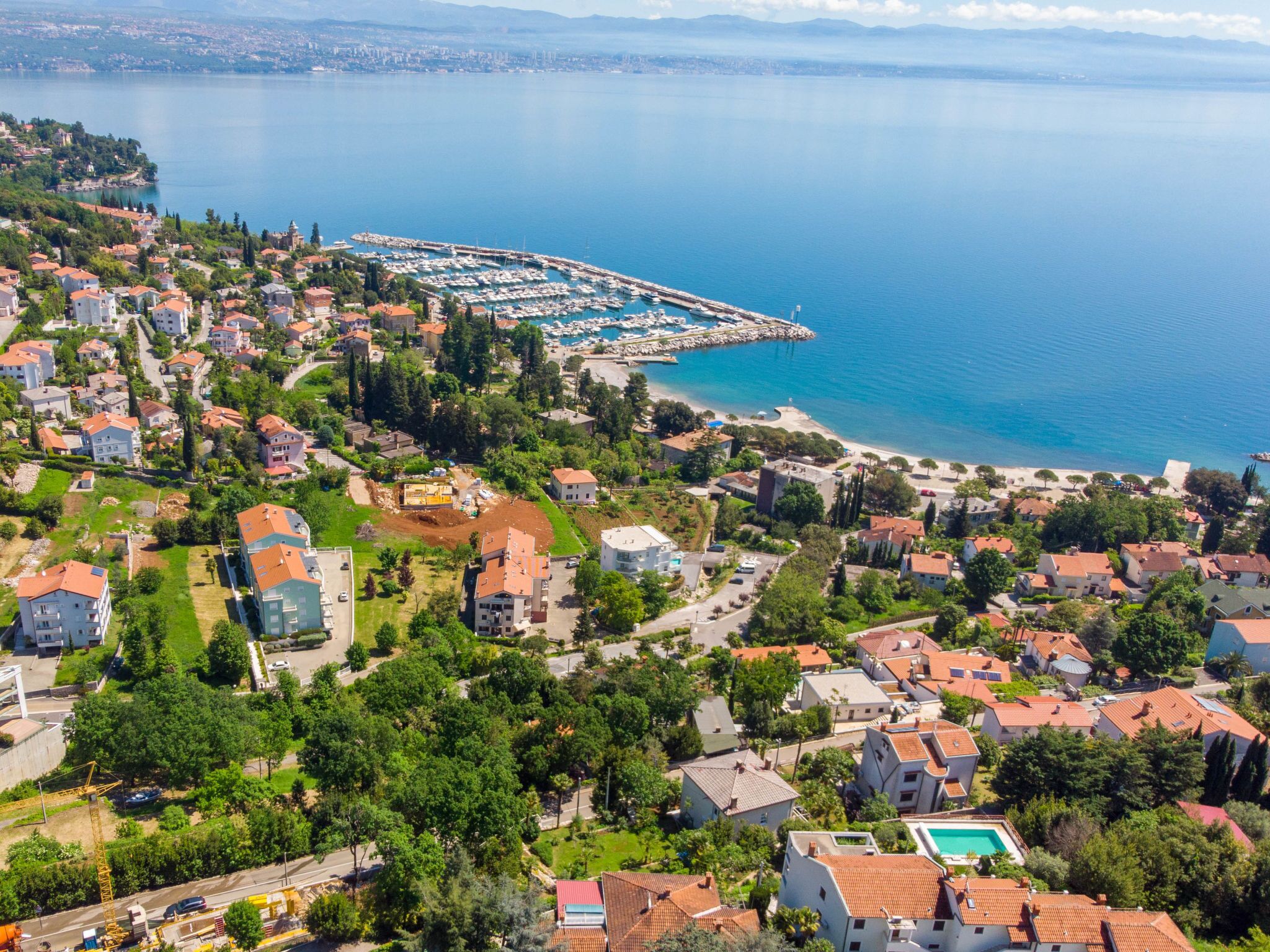 Una vista aerea di una zona residenziale costiera con case, un porto turistico e una spiaggia.