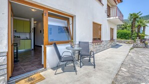 A modern building with a patio area featuring a table and chairs, a visible kitchen, and a stone wall.