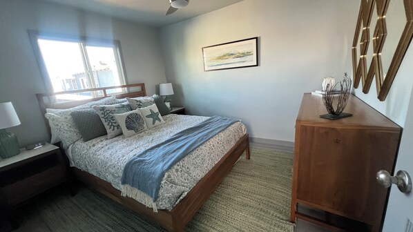 Een slaapkamer met een bed, nachtkastjes, een dressoir, een ingelijst schilderij aan de muur en een raam met jaloezieën.