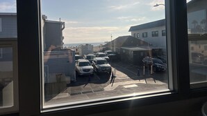 Vista desde una ventana sobre un estacionamiento con varios autos, una playa al fondo y edificios de estilo arquitectónico moderno.