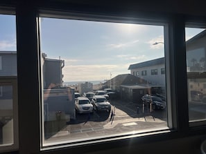 Blick aus einem Fenster auf einen Parkplatz mit mehreren Autos, im Hintergrund ein Strand und Gebäude im modernen Architekturstil.