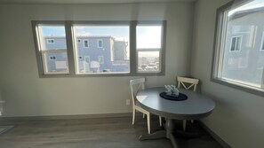 Ein Zimmer mit einem runden Tisch und zwei Stühlen, großen Fenstern mit Blick auf Gebäude und einer weißen Wand.