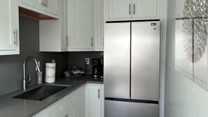 Una cocina moderna con armarios blancos, un refrigerador de acero inoxidable, una cafetera y un adorno en la pared.