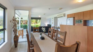 Une cuisine moderne avec des meubles en bois, un coin repas avec une longue table et des chaises, et une grande fenêtre offrant une vue sur l’extérieur.