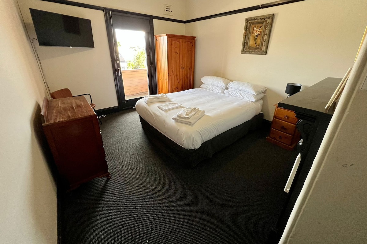 A hotel room with a bed, a desk, a chair, a wardrobe, and a television on the wall.