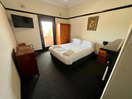 Habitación de hotel con cama, escritorio, silla, armario y televisor en la pared.