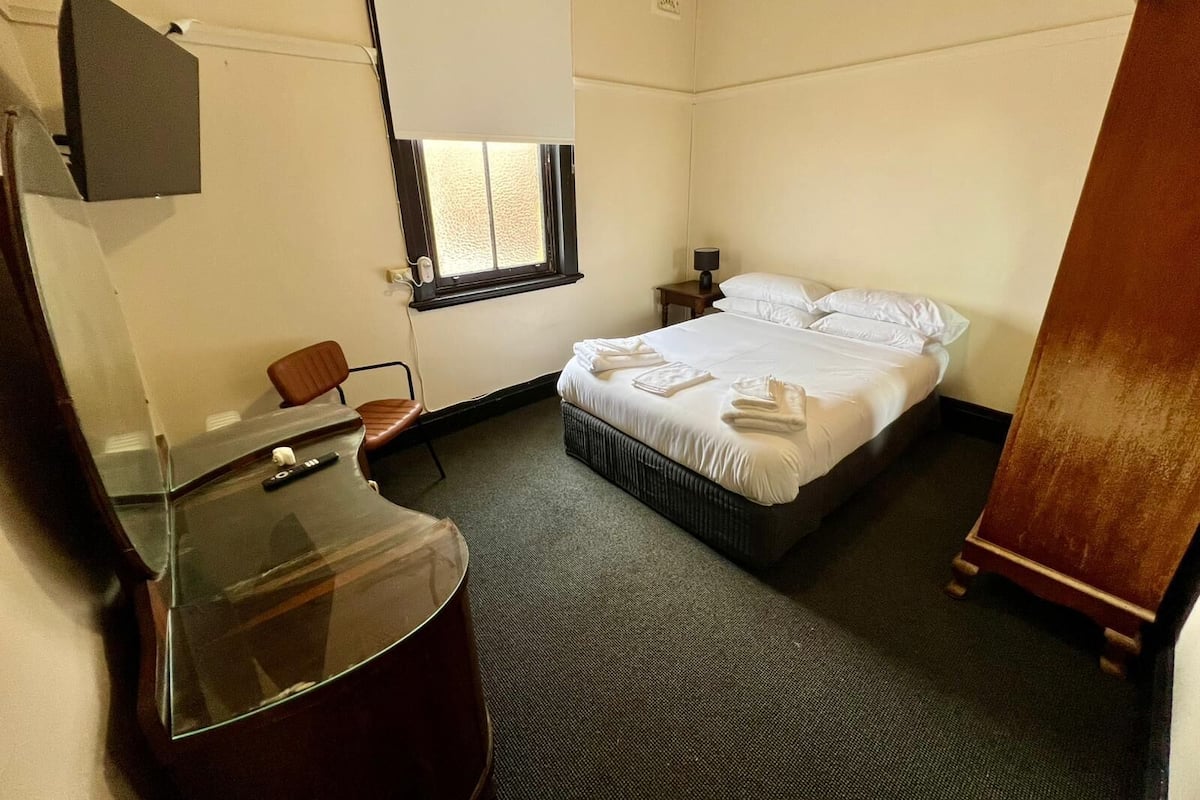 A hotel room with a bed, a desk with a chair, a TV mounted on the wall, and a window with a view.