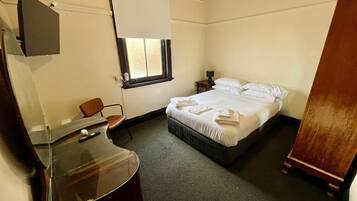 A hotel room with a bed, a desk with a chair, a TV mounted on the wall, and a window with a view.