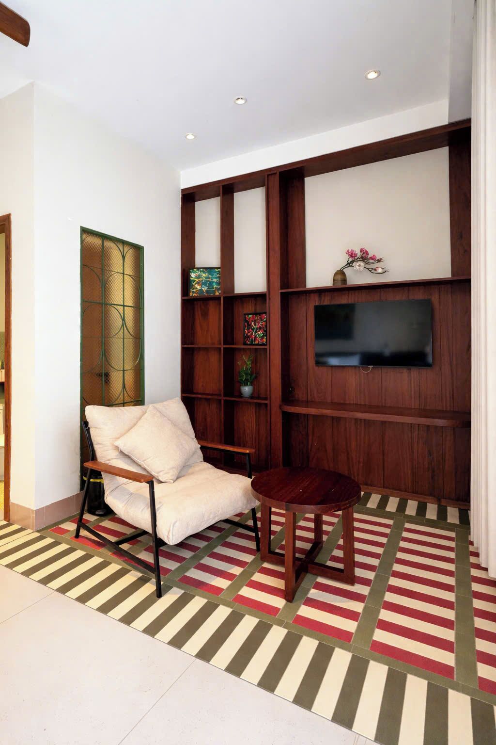 A living room with a sofa, a small round table, a TV mounted on a wooden wall, and a patterned rug.