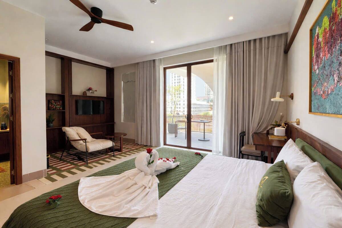 A hotel room with a bed, a chair, a desk, a television, a ceiling fan, and a view of the outside.