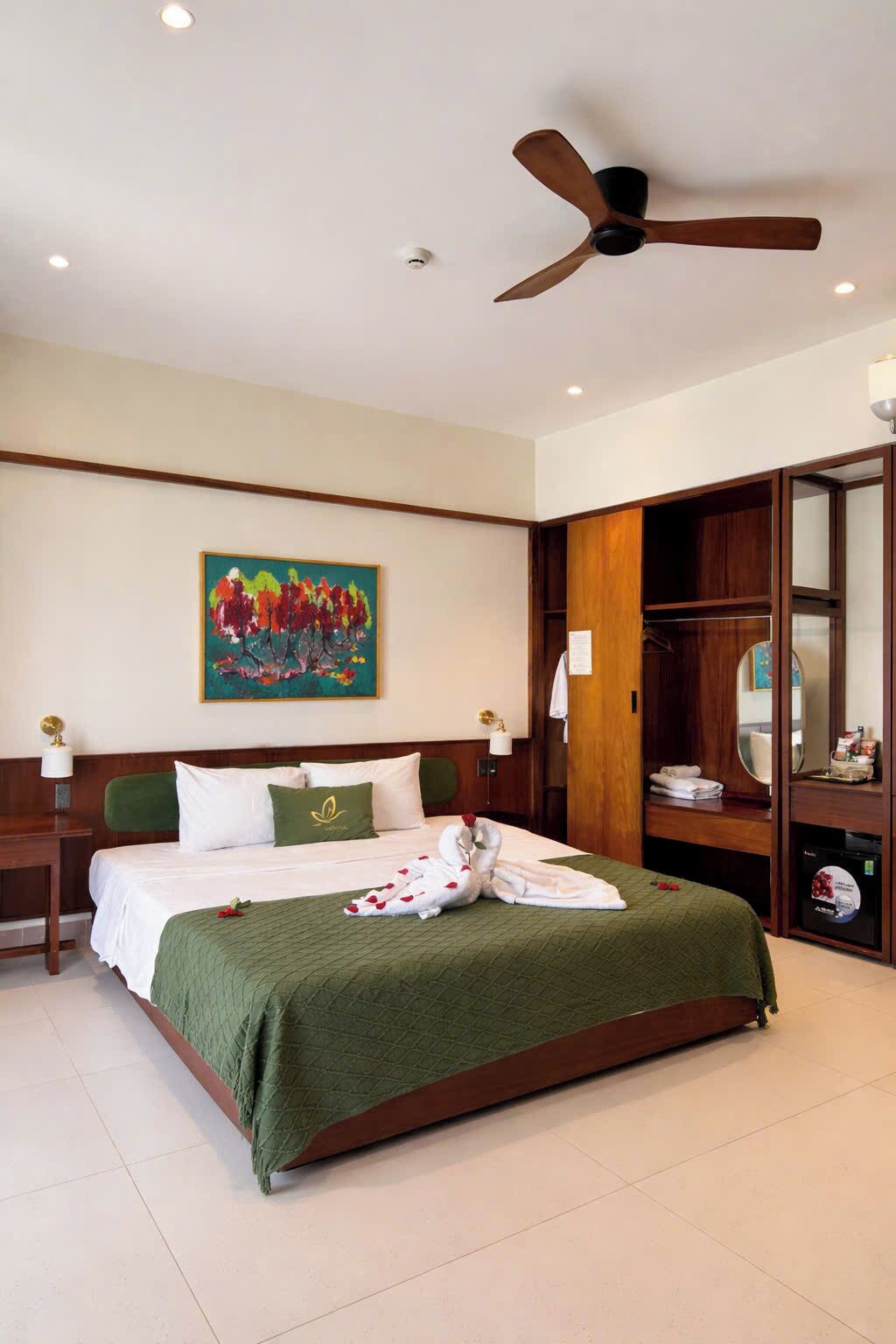 A hotel room with a bed, a ceiling fan, a painting, a wardrobe, and a bedside table.