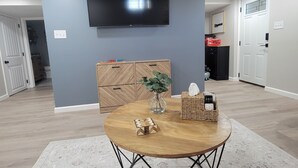 Ein modernes Wohnzimmer mit einem runden Holztisch, einem Flachbildfernseher an der Wand und einem Schrank mit Fischgrätmuster.