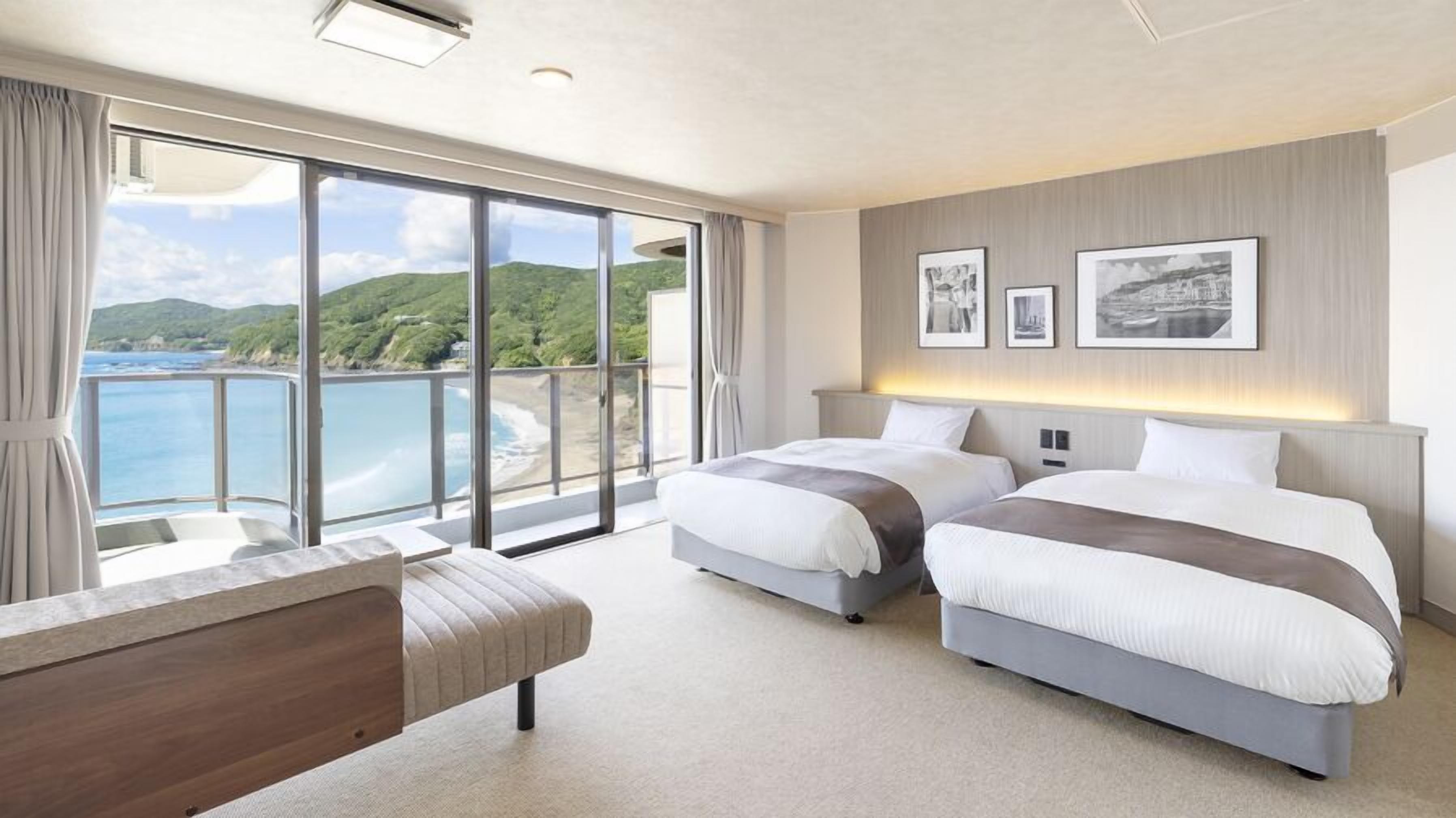 Una habitación de hotel moderna con dos camas, un ventanal con vistas al mar y un balcón.
