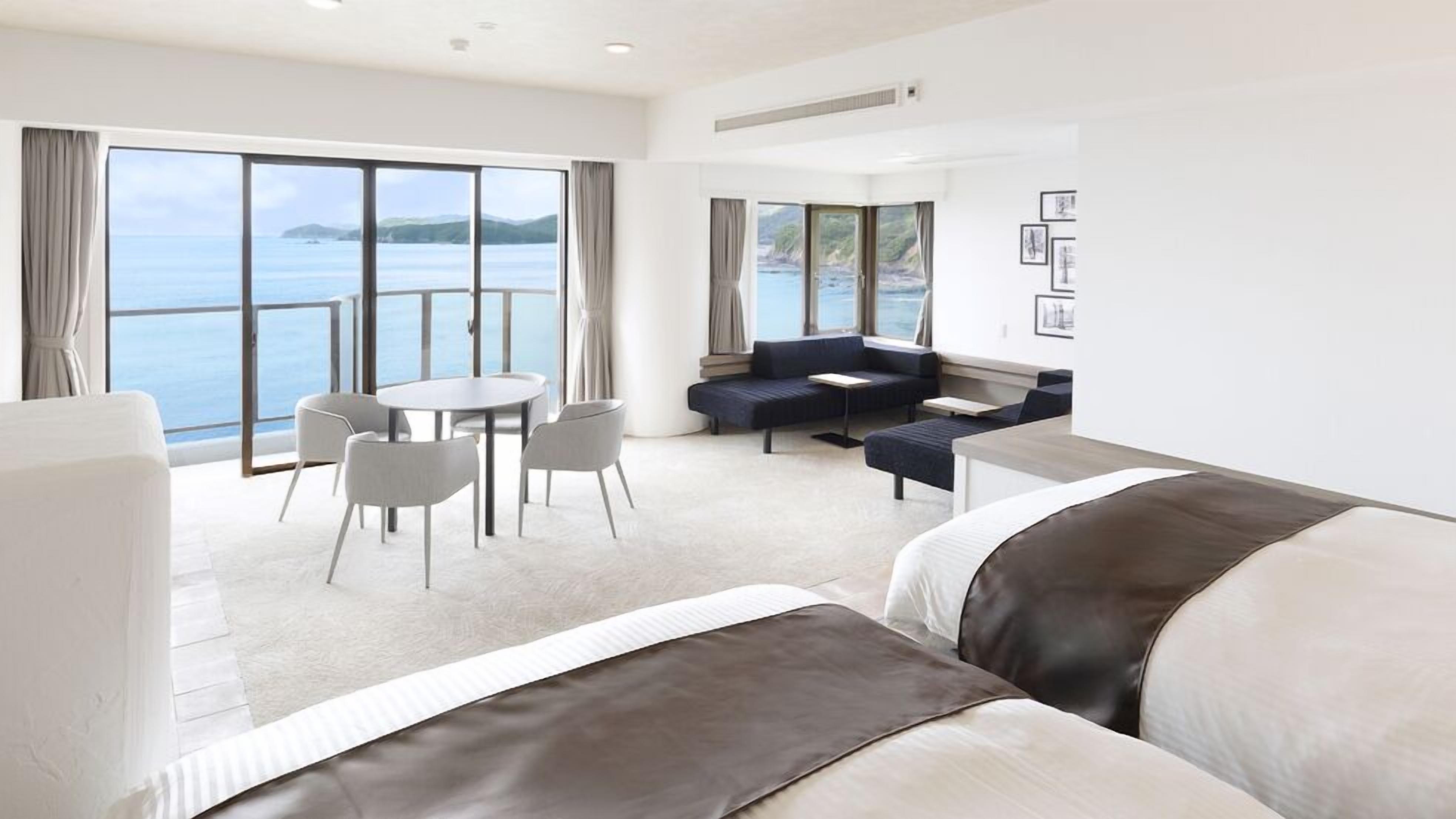 Una habitación de hotel moderna con un ventanal grande, un sofá, una mesa de comedor con sillas y una cama.