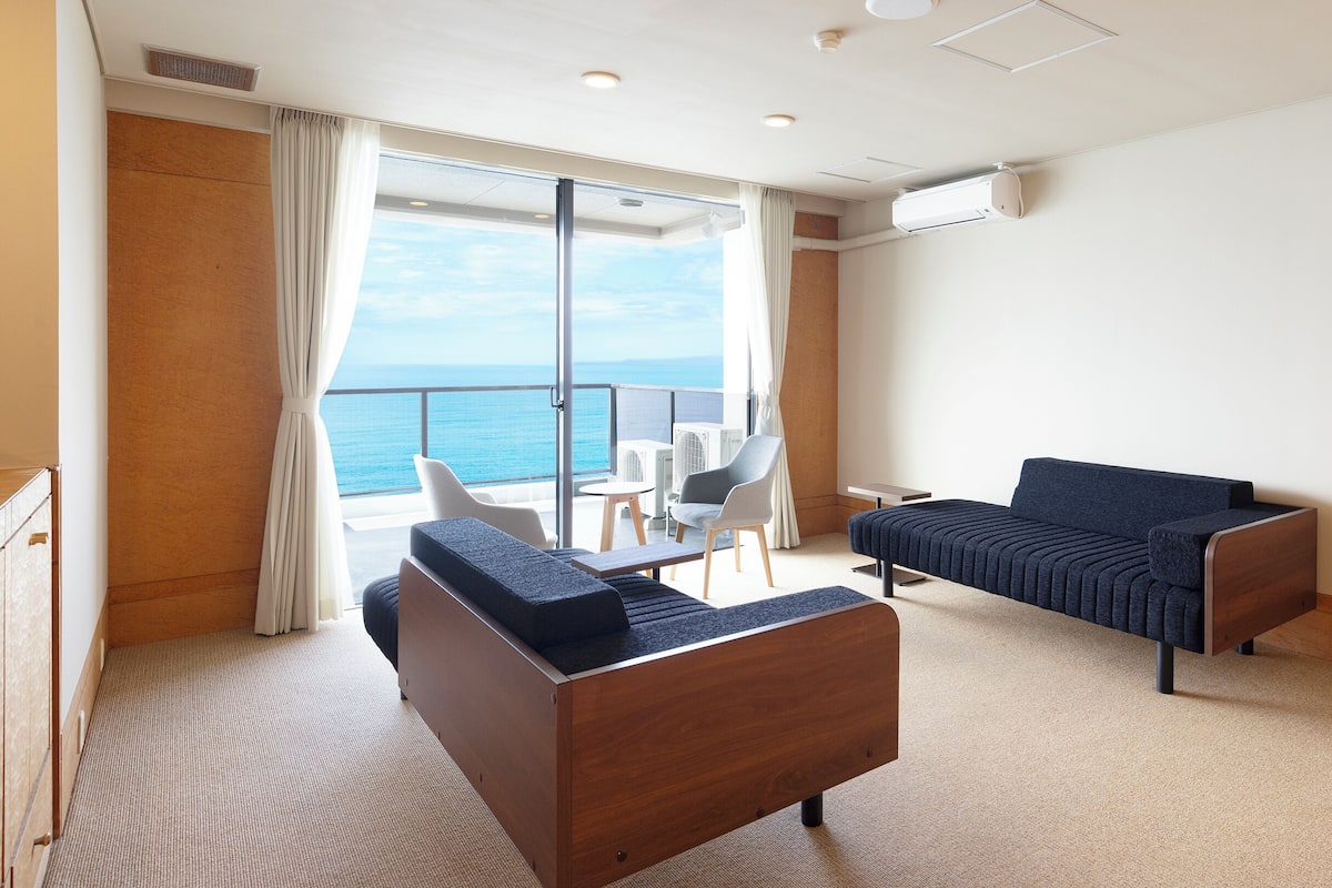 A modern hotel room with a balcony, a sofa, a chair, and a small table.