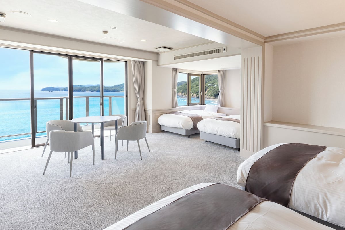 A hotel room with a large balcony, a dining area, and two beds.