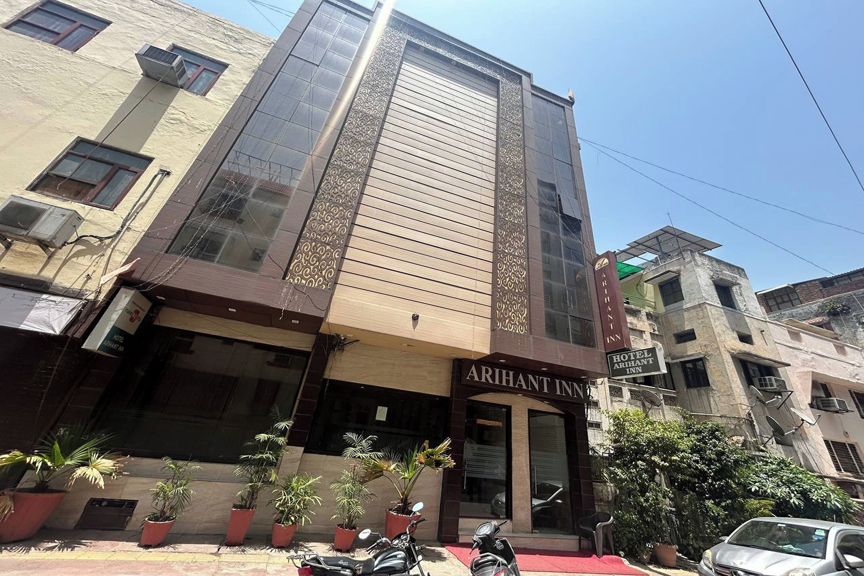 A hotel named "Arihant Inn" with a modern facade, large windows, and potted plants in front.