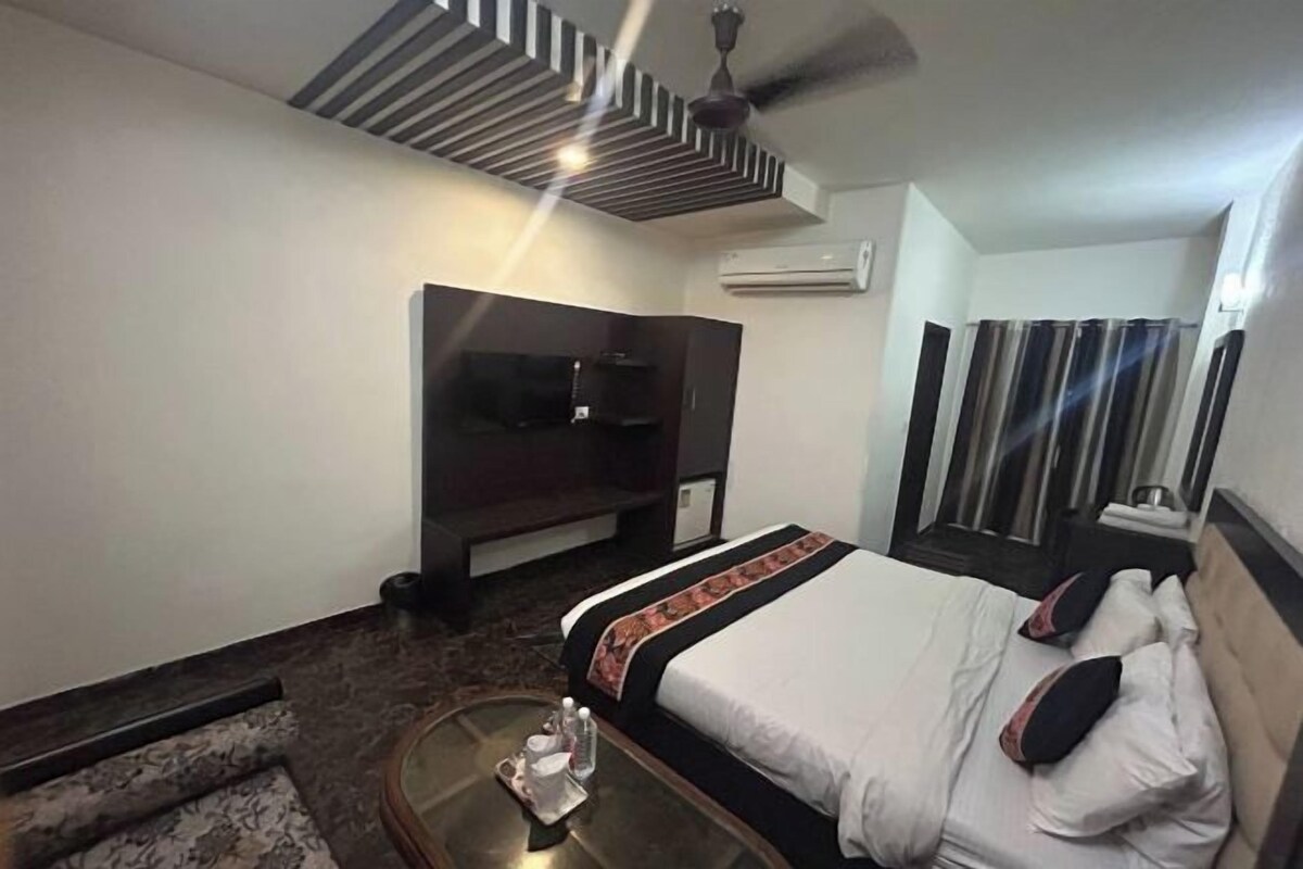 A hotel room with a bed, a TV, a ceiling fan, and an air conditioning unit.