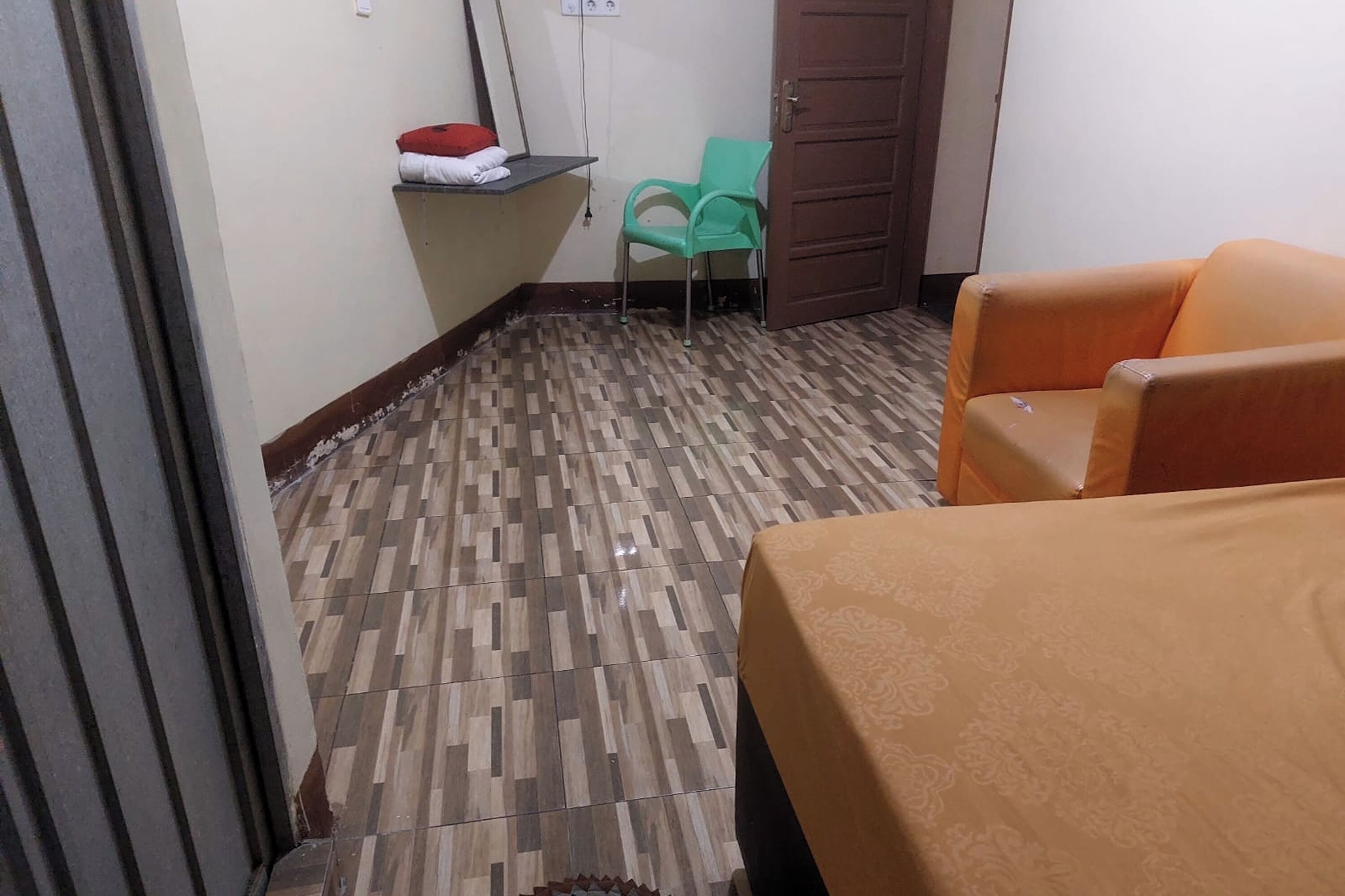 Una habitación de hotel con piso estampado, una cama con colcha naranja, una silla verde y una puerta de madera.