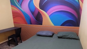 A room with a bed, two pillows, a chair, and a colorful mural on the wall. - Hotel Warna (Palopo)