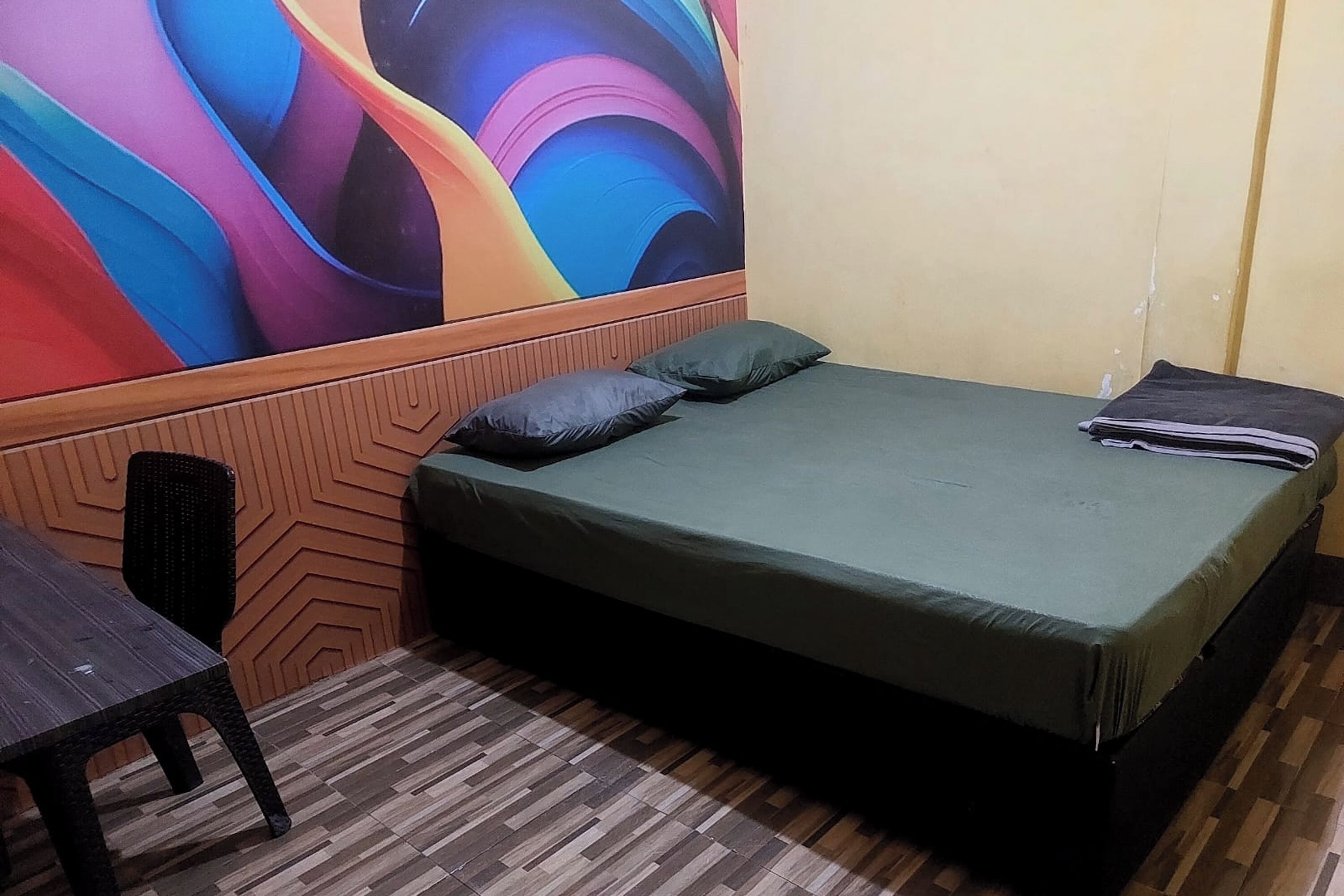 A room with a bed, a chair, and a colorful abstract mural on the wall.