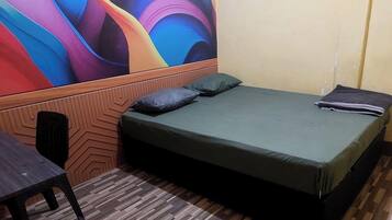A room with a bed, a chair, and a colorful abstract mural on the wall.