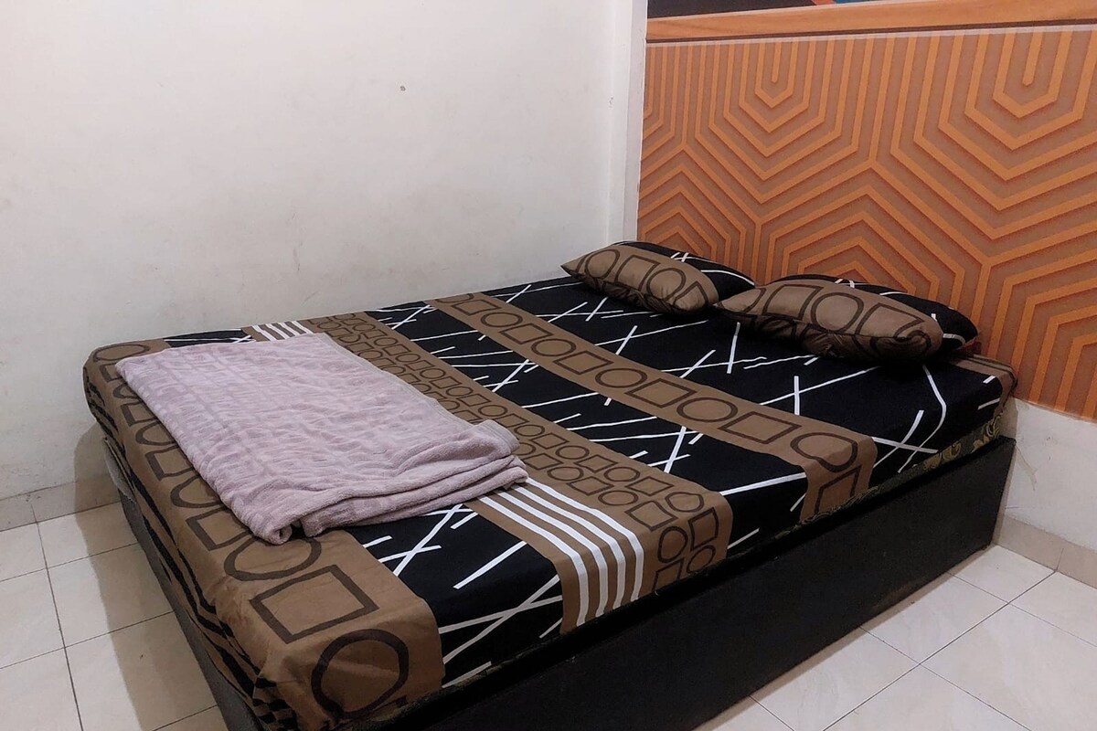 A bed with a patterned bedspread, pillows, and a folded blanket.