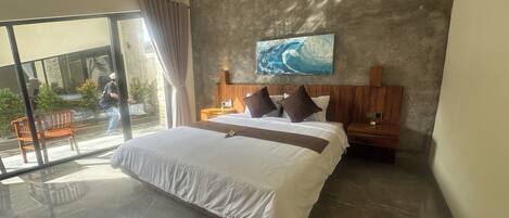 Una habitación de hotel moderna con una cama grande, un cabecero de madera, un cuadro de una ola y un balcón con vistas.