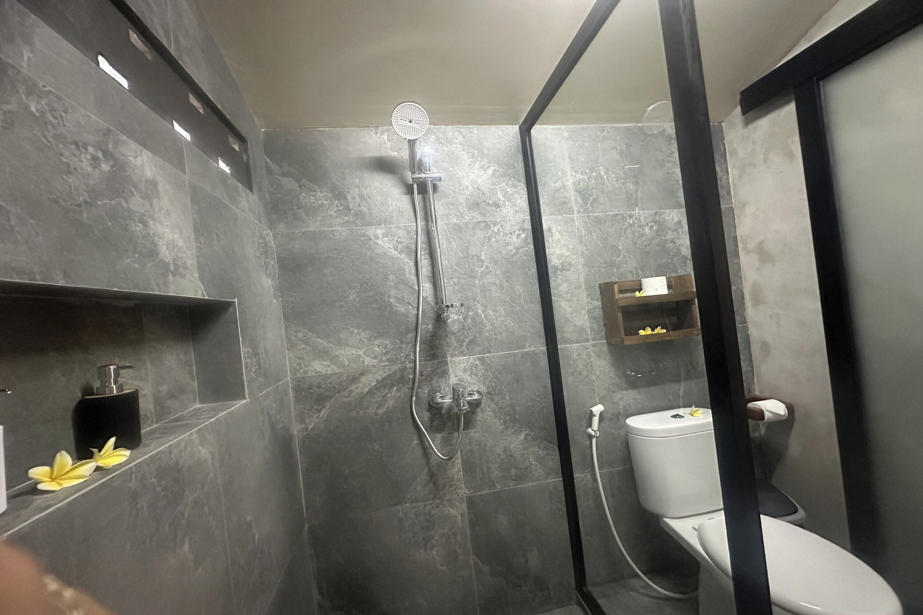 Et moderne badeværelse med et glasafskærmet brusebad, toilet og en hylde med toiletartikler.