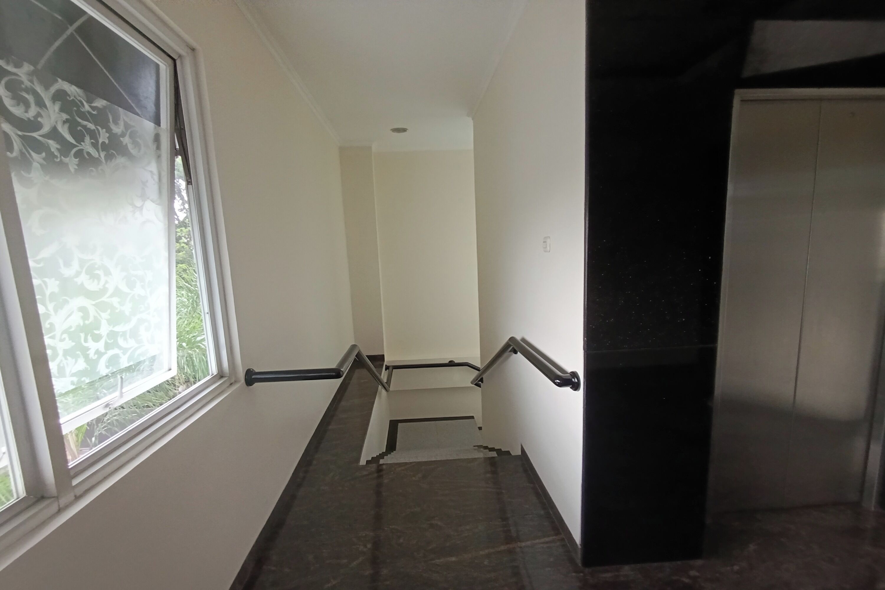 A narrow stairway with a handrail, a window with frosted glass, and a door at the top.