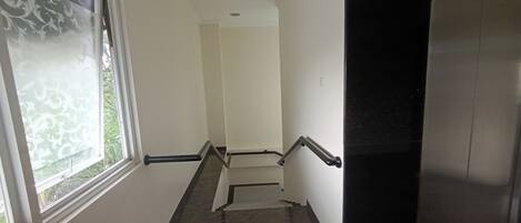 A narrow stairway with a handrail, a window with frosted glass, and a door at the top.