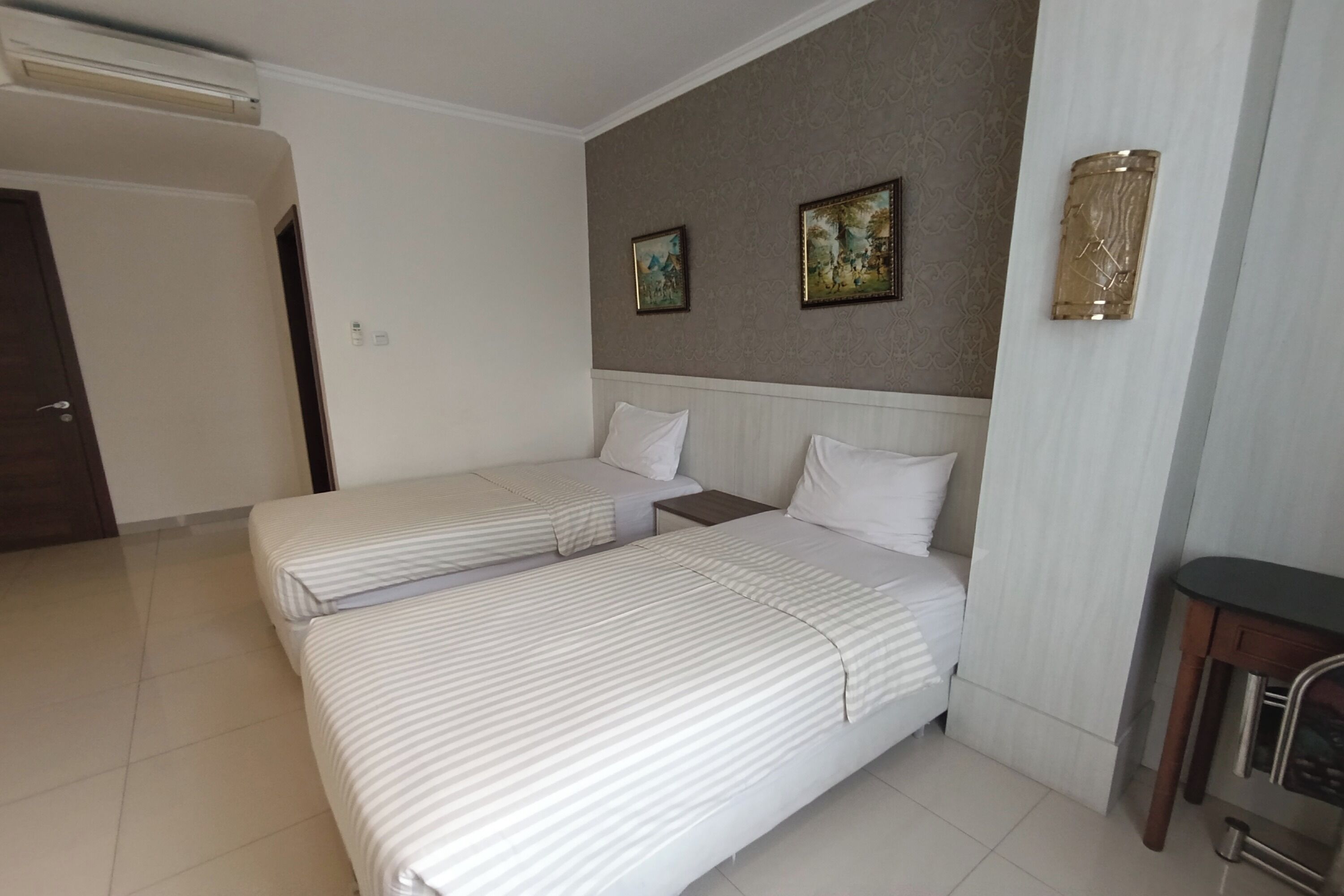 Camera d'albergo con due letti singoli, un comodino, una lampada a parete e due quadri incorniciati.