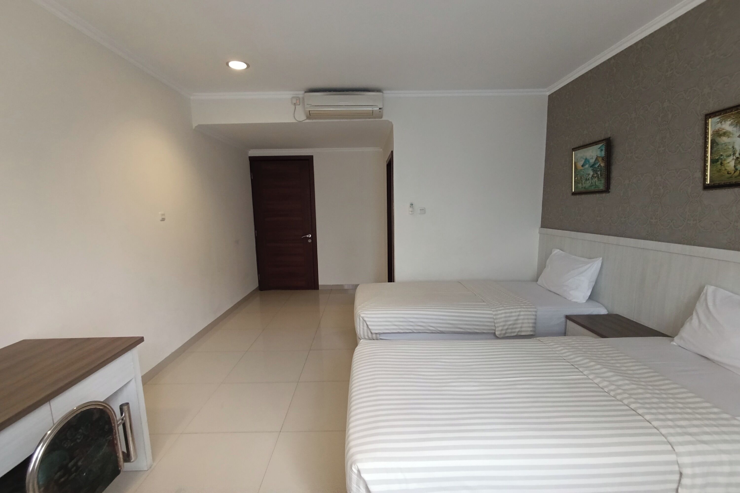 Habitación de hotel con dos camas, una mesita de noche de madera, una pequeña mesa y un equipo de aire acondicionado en el techo.