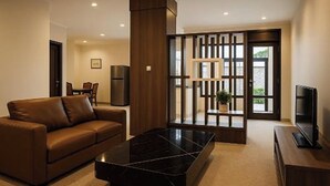 A modern living room with a brown leather sofa, a black marble coffee table, and a television on a wooden stand. - Cipto Apartment (Bandung)