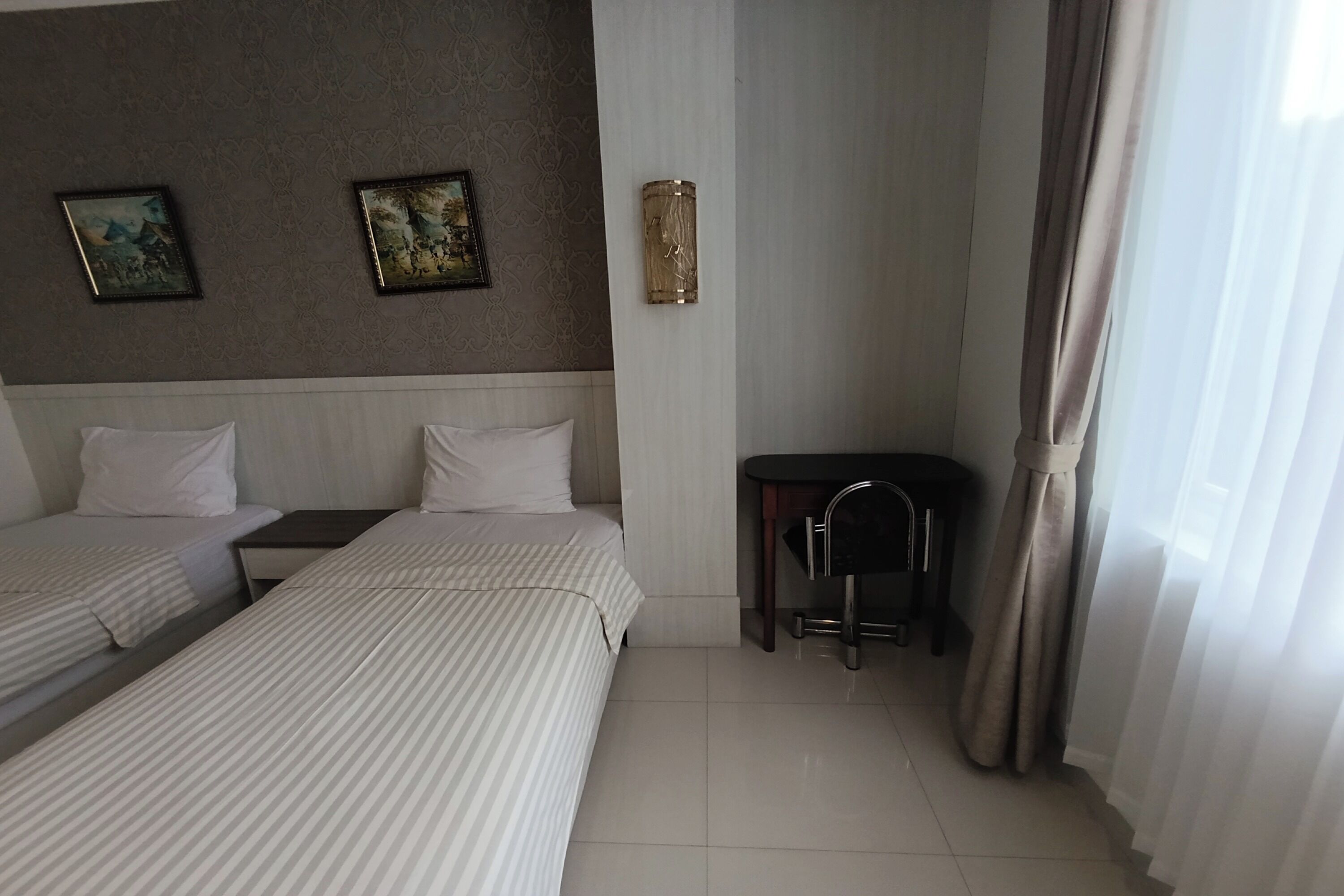 Habitación de hotel con dos camas, un escritorio pequeño, una silla y una lámpara de pared.