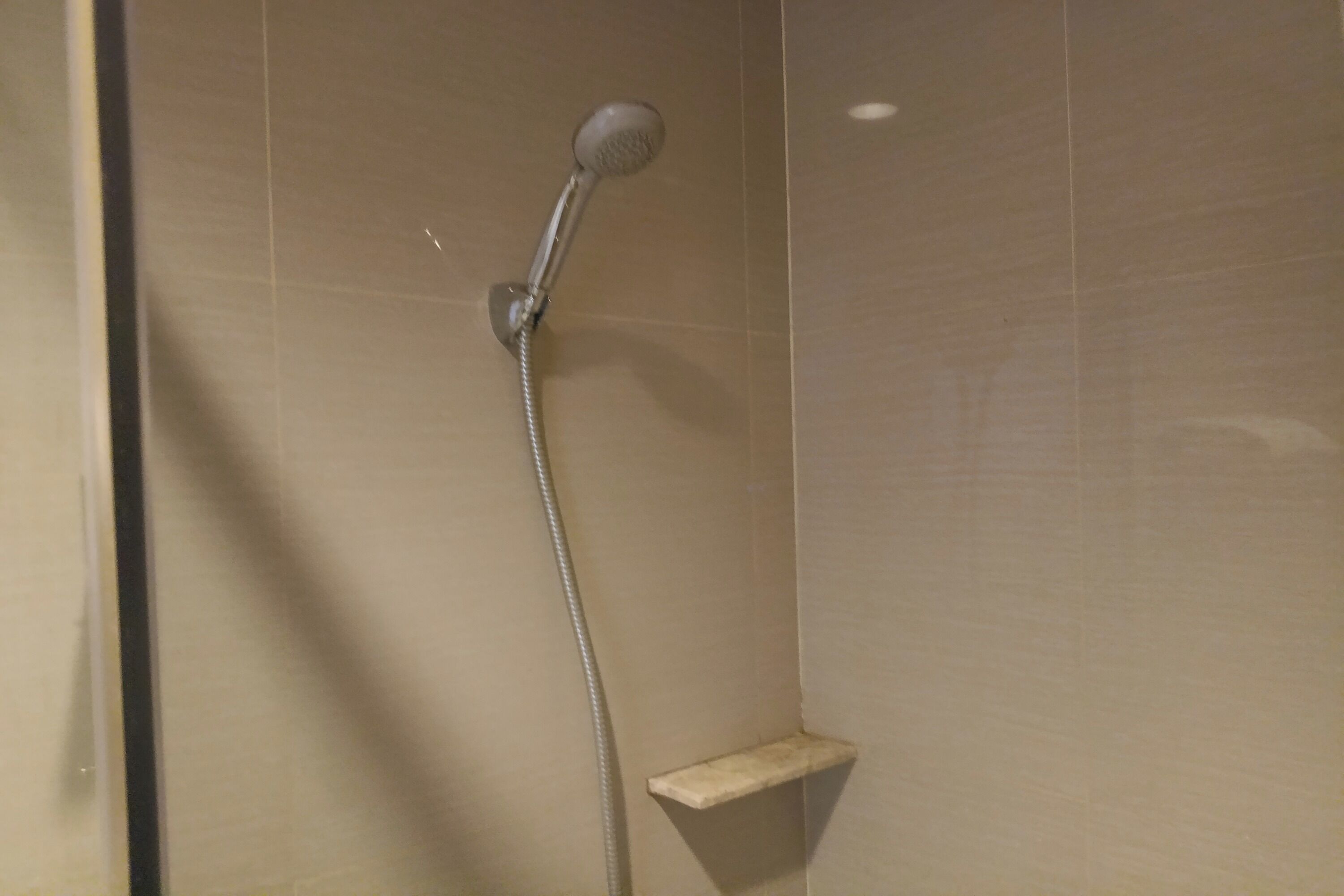 A shower with a handheld showerhead and a wall-mounted control panel.