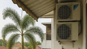 A balcony with air conditioning units, a palm tree, and a view of a residential area. - Cipto Apartment (Bandung)